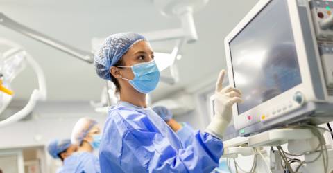 Jonge vrouwelijke arts in operatiekleding en een beschermend gezichtsmasker dat een anesthesiemachine voorbereidt voor een operatie